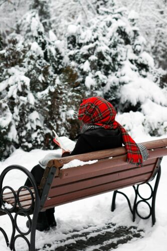 A person enjoys reading on a snowy park bench in winter, Ankara, Türkiye.