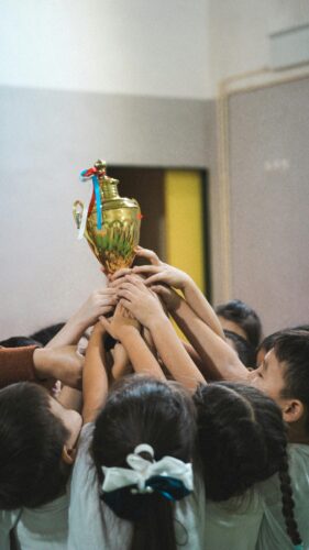 Group of children lifting a golden trophy indoors celebrating achievement and teamwork.